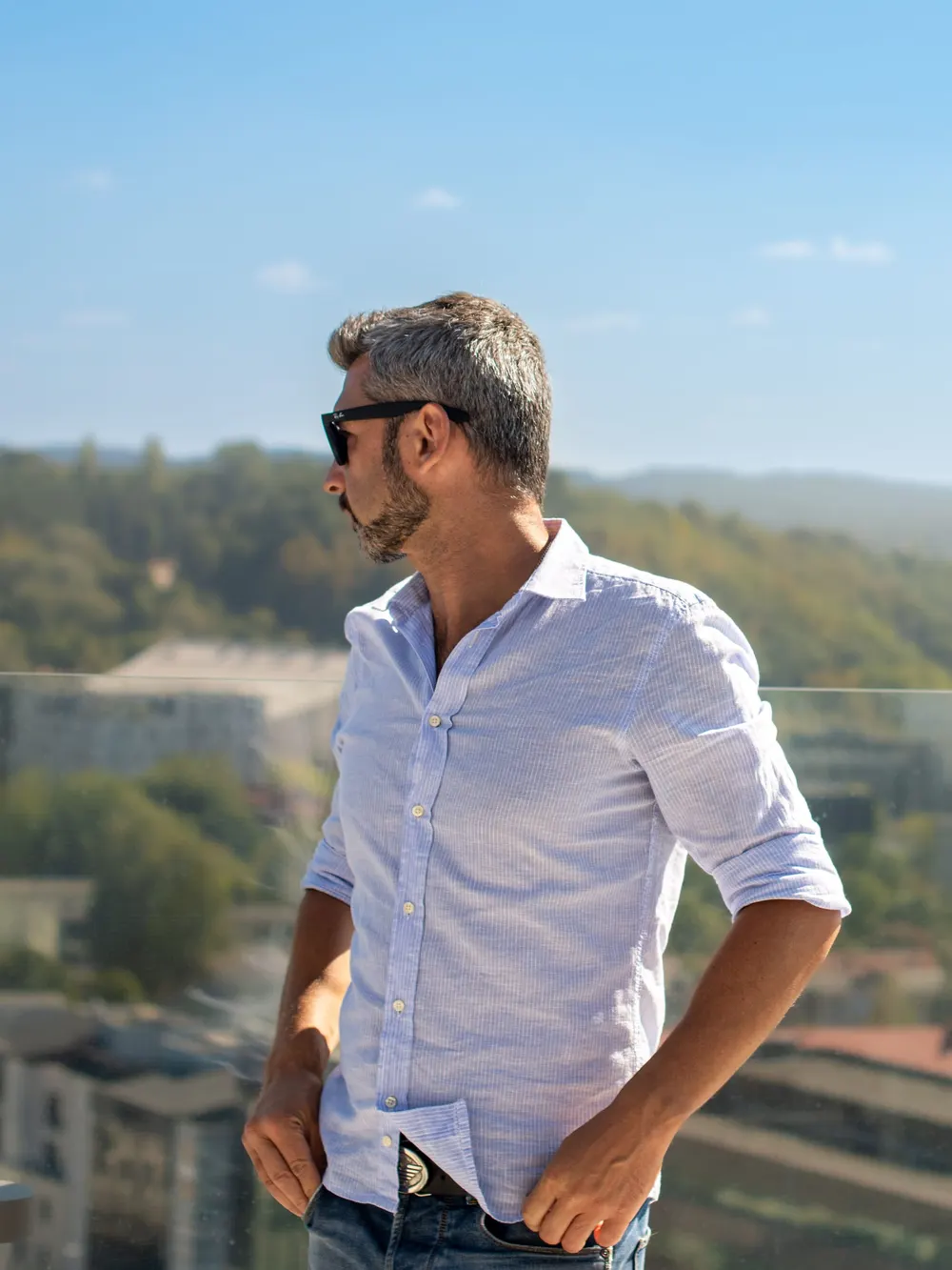 Man in a white linen shirt and sunglasses looking out over green hills