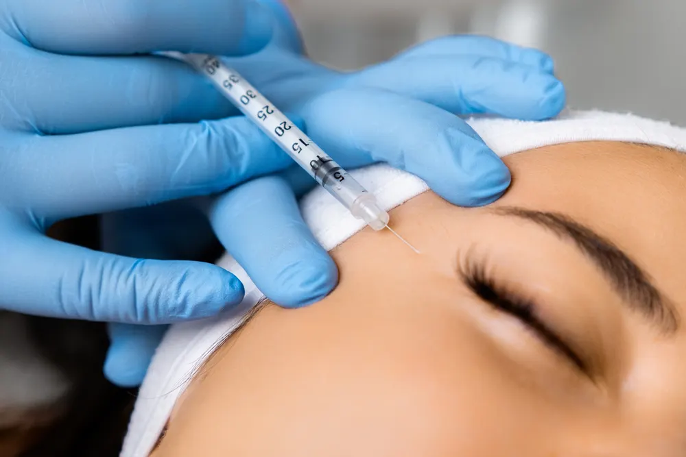 Gloved hands giving a Botox injection to a patient’s forehead